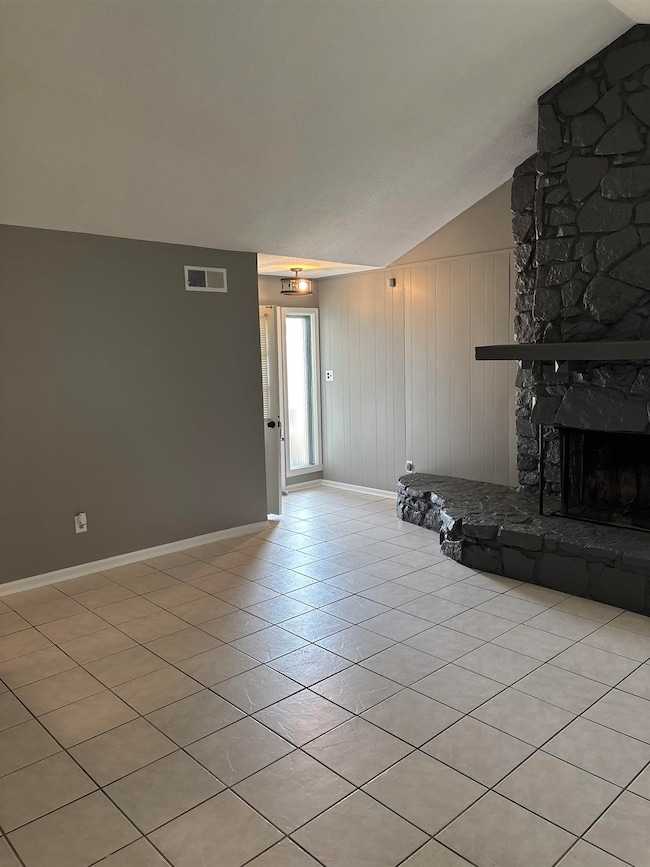 Unfurnished living room with lofted ceiling, baseboards, light tile patterned flooring, and a stone fireplace