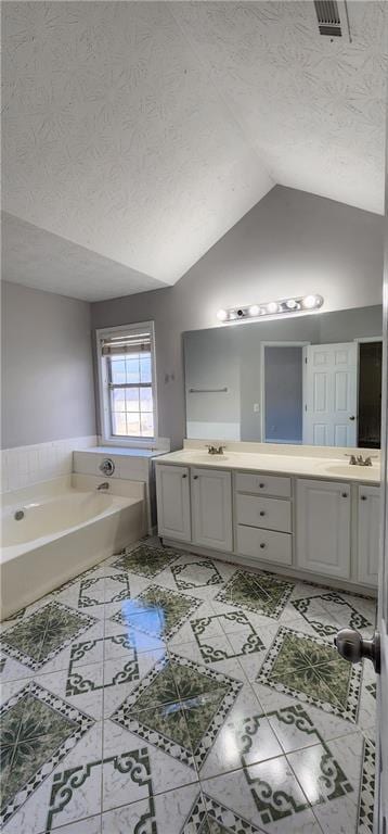 Bathroom with a textured ceiling, lofted ceiling, double vanity, and a garden tub