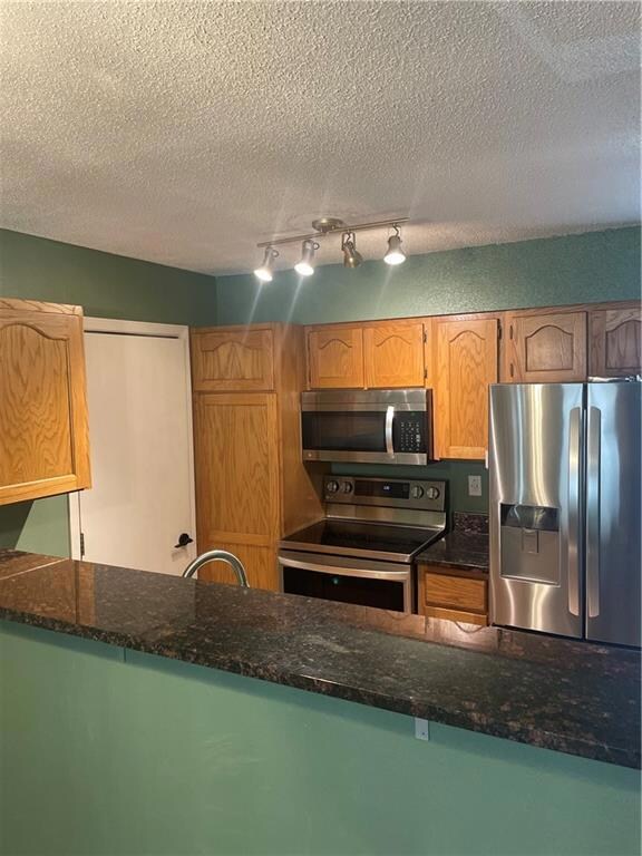 Kitchen with fridge, dark stone counters, rail lighting, range, and a textured ceiling