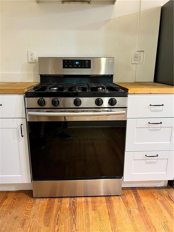 Kitchen featuring stainless steel range with gas stovetop, wooden counters, white cabinetry, and light wood-type flooring