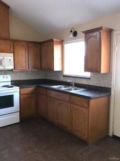 Kitchen featuring white appliances, dark countertops, vaulted ceiling, and brown cabinetry