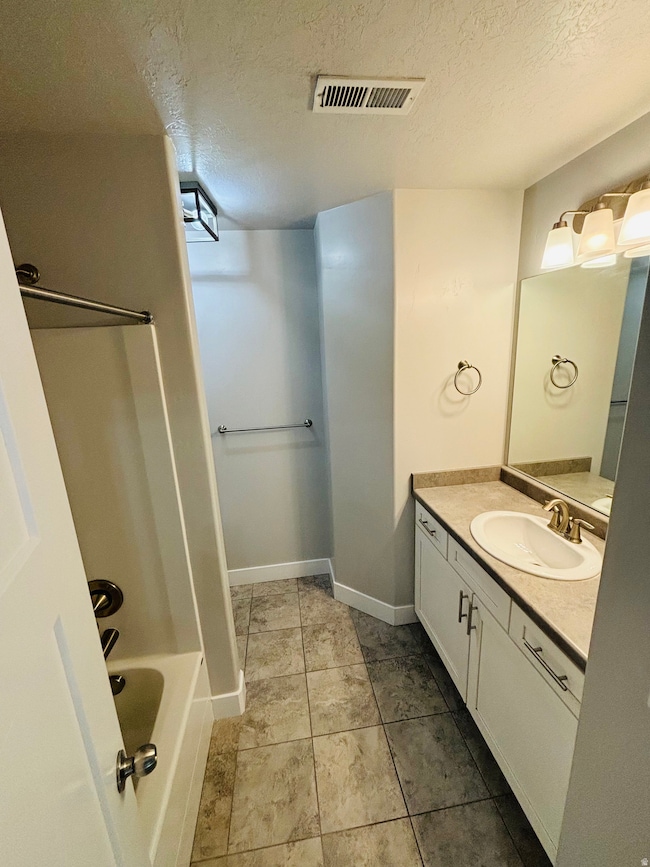 Full bathroom featuring a textured ceiling, vanity,  shower combination, and light tile patterned floors