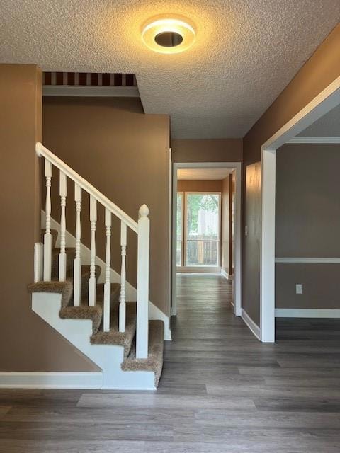 Staircase featuring a textured ceiling and wood finished floors