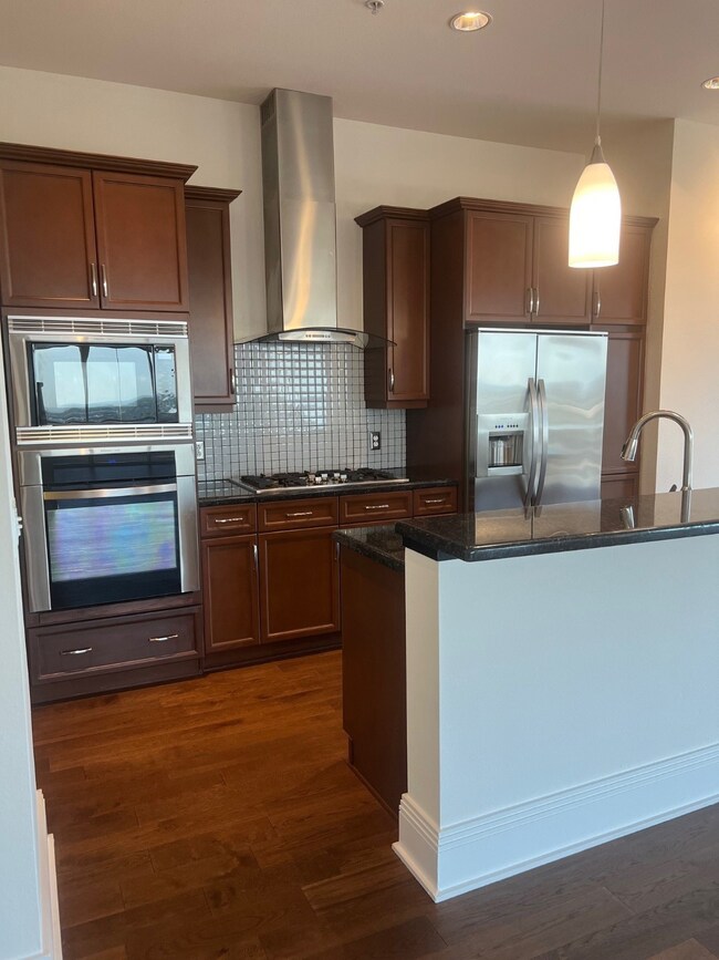 Kitchen with cooktop, ventilation hood, dark stone counters, fridge, and wall oven