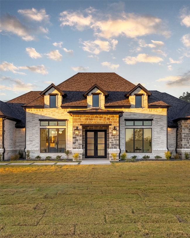 Back of house featuring a lawn, brick siding, french doors, and roof with shingles
