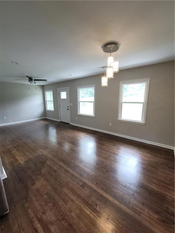 Unfurnished living room featuring a chandelier, dark wood finished floors, and ceiling fan