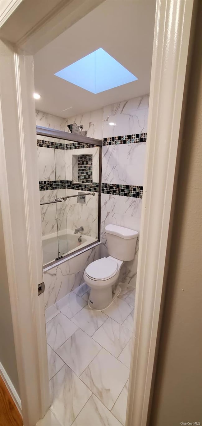 Bathroom featuring a skylight, tiled shower / bath combo, light marble finish flooring, and tile walls