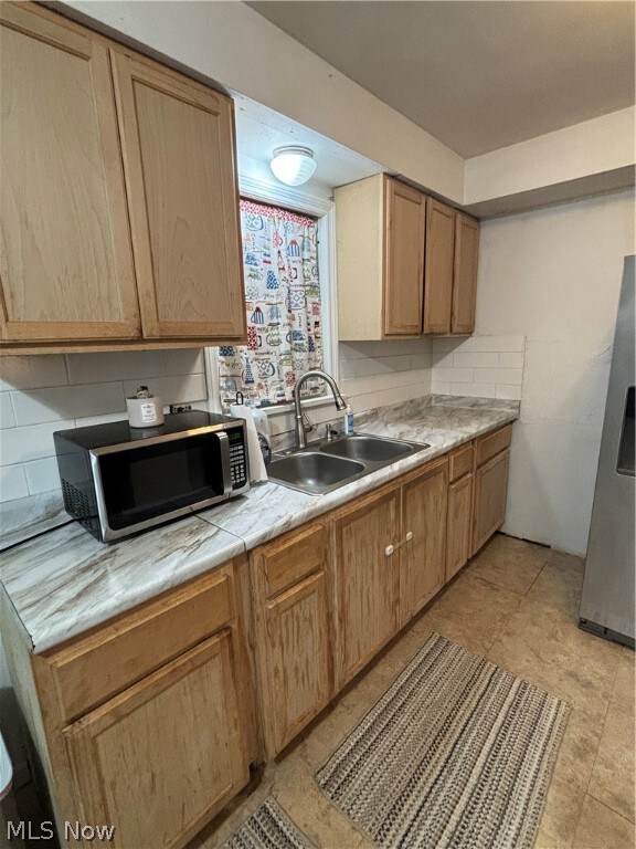 Kitchen with fridge, sink, backsplash, and light tile flooring
