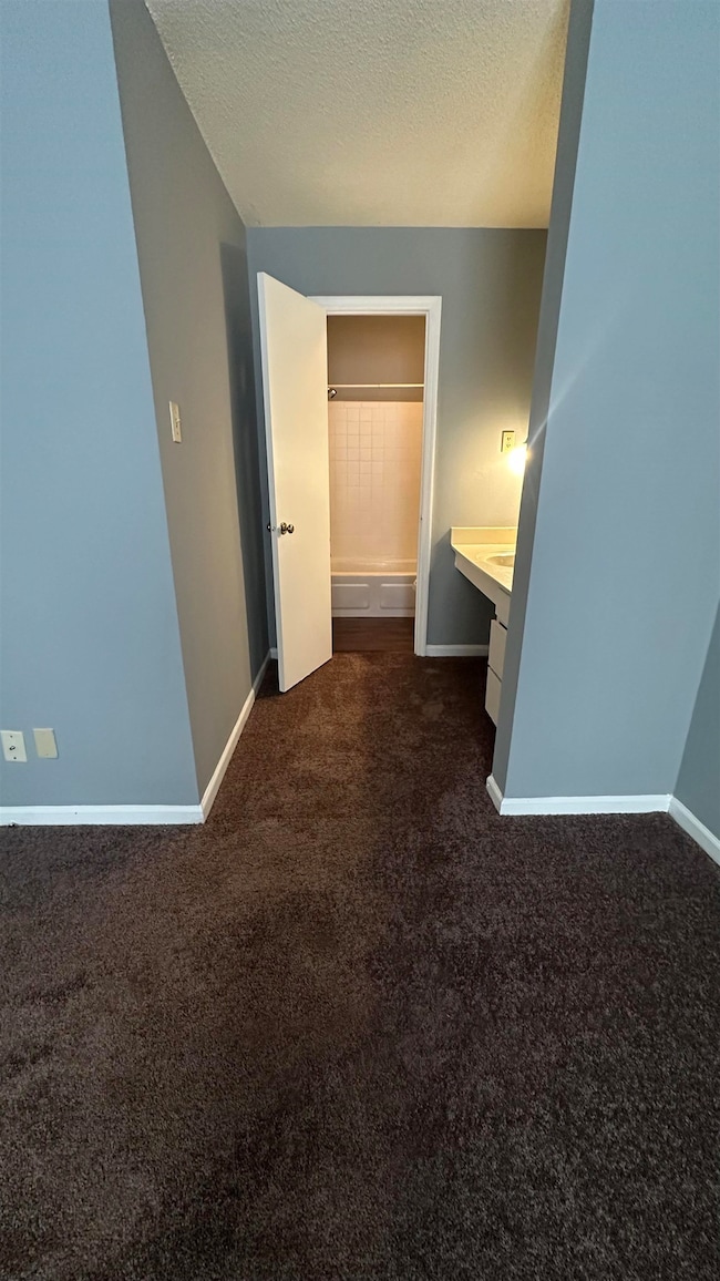 Corridor featuring baseboards, dark carpet, and a 