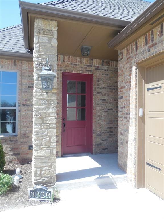Doorway to property with brick siding, a shingled roof, and a garage