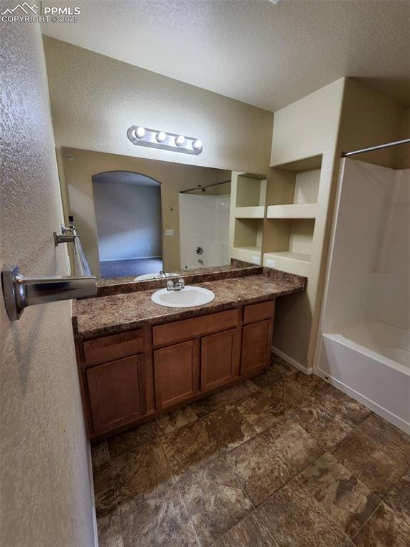 Bathroom featuring a textured ceiling, a textured wall, shower / bath combination, and vanity