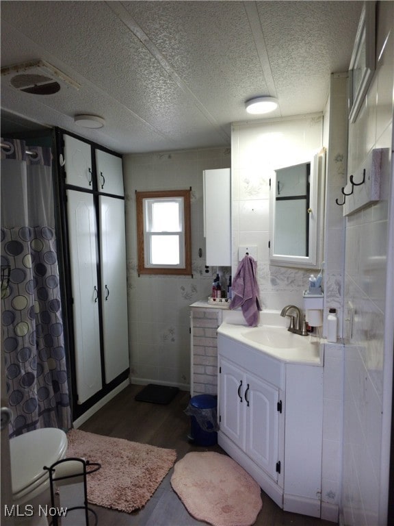 Full bathroom with tile walls, vanity, dark wood finished floors, a textured ceiling, and a shower with curtain