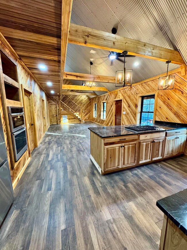 Kitchen featuring wooden walls, dark countertops, dark wood-type flooring, appliances with stainless steel finishes, and pendant lighting