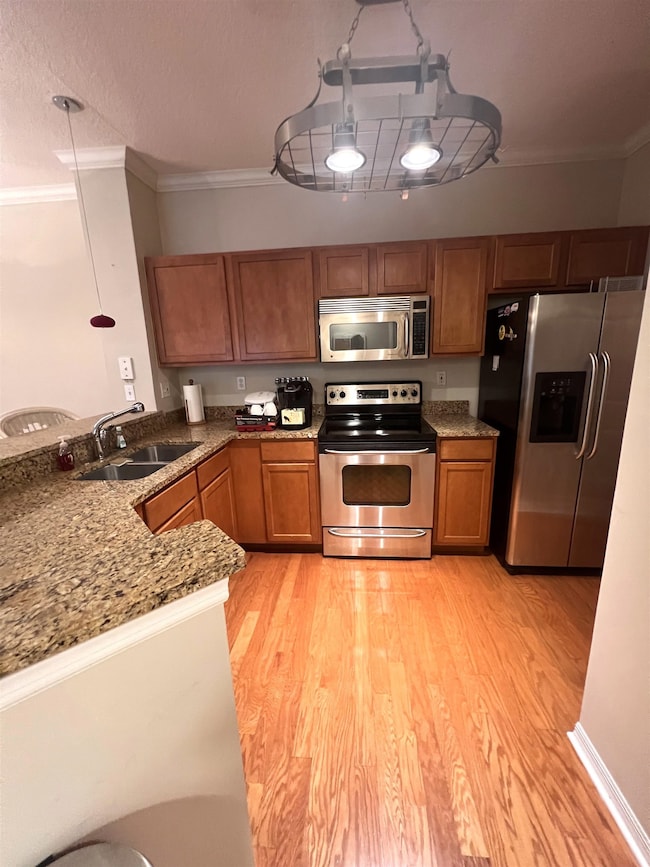 Kitchen with stainless steel appliances, ornamental molding, brown cabinets, light stone counters, and a textured ceiling