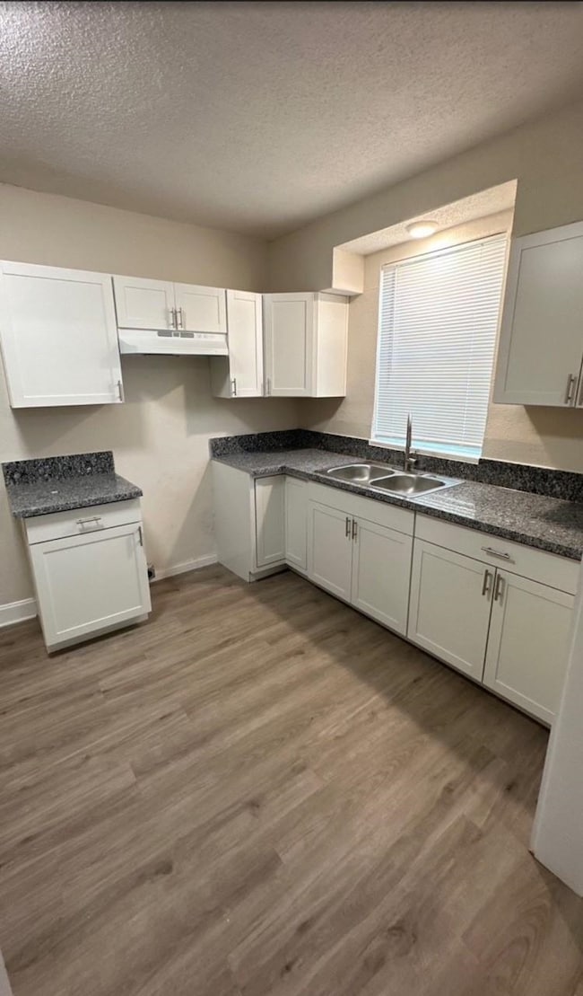 Kitchen with a textured ceiling, light wood-style floors, white cabinetry, and under cabinet range hood