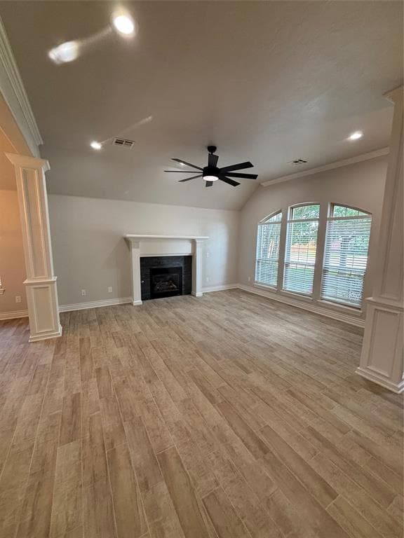 Unfurnished living room featuring ornate columns, ceiling fan, crown molding, a fireplace, and light wood-style floors