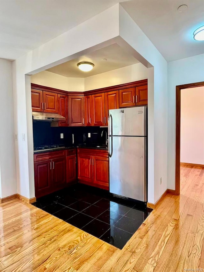 Kitchen with freestanding refrigerator, dark brown cabinets, under cabinet range hood, black gas cooktop, and tasteful backsplash