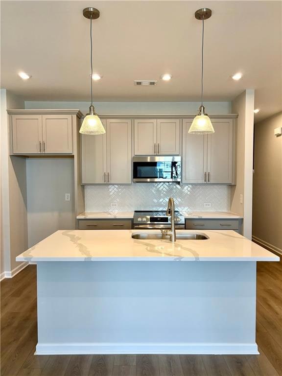 Kitchen with stainless steel microwave, gray cabinets, a kitchen island with sink, visible vents, and a sink