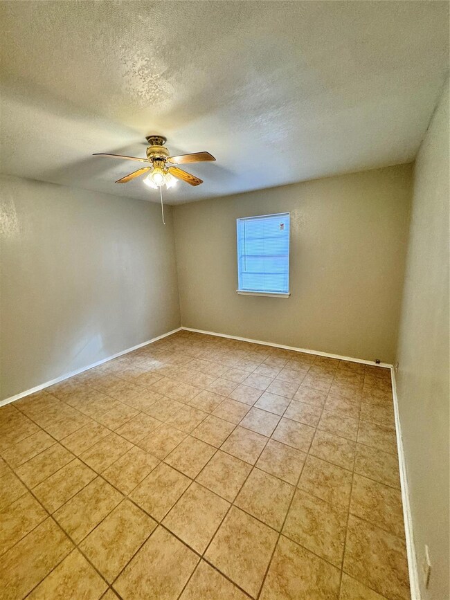 Tiled spare room with ceiling fan and a textured c