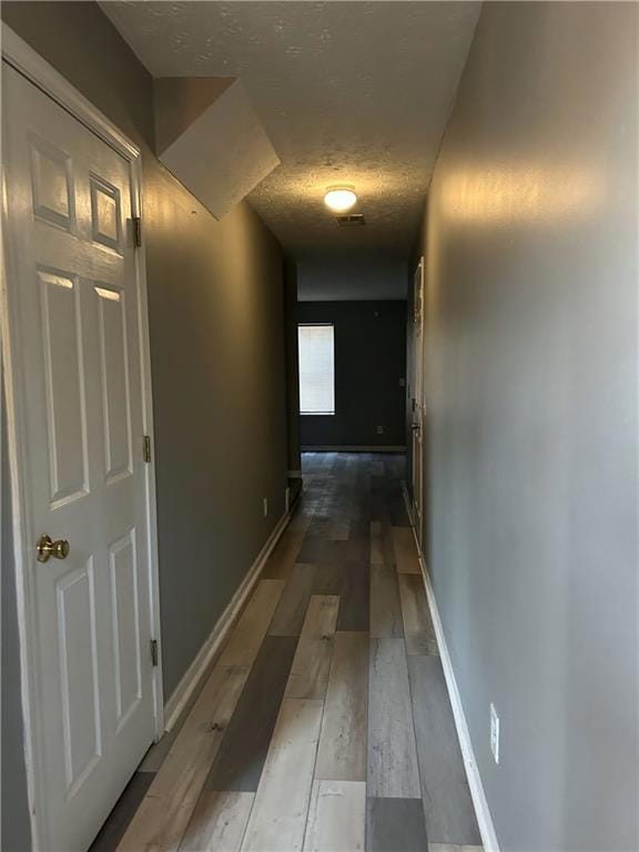 Corridor with a textured ceiling, baseboards, and 