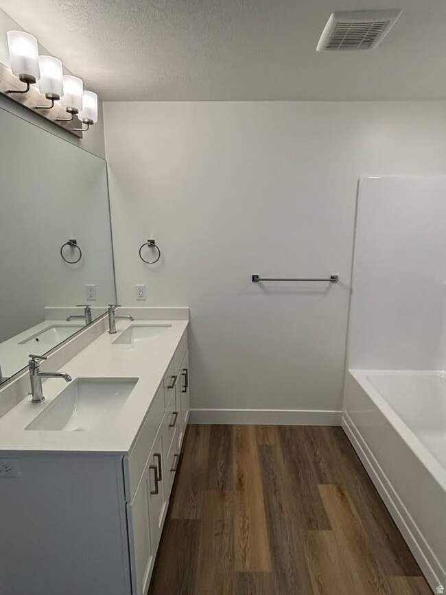 Full bath featuring double vanity, dark wood finished floors, a textured ceiling, and bathing tub / shower combination