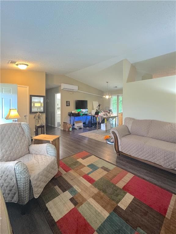 Living area with wood finished floors, lofted ceiling, a wall mounted AC, a chandelier, and a textured ceiling