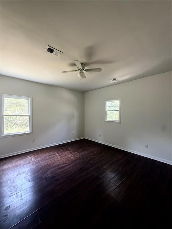 Empty room with healthy amount of natural light, baseboards, dark wood finished floors, and a ceiling fan