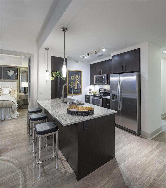 Kitchen with light hardwood / wood-style flooring, hanging light fixtures, light stone countertops, appliances with stainless steel finishes, and sink