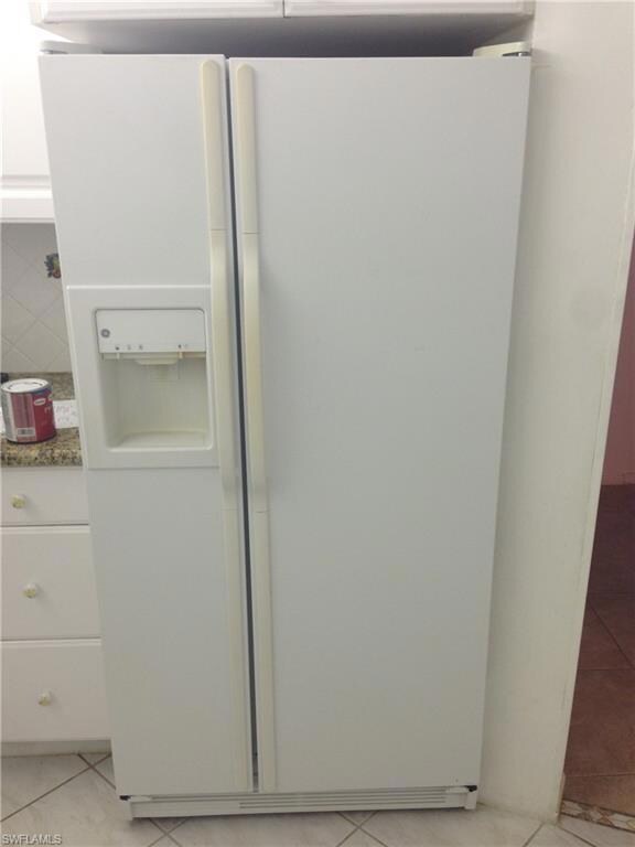 Kitchen view of white fridge with ice dispenser, white cabinetry, decorative backsplash, and dark stone countertops