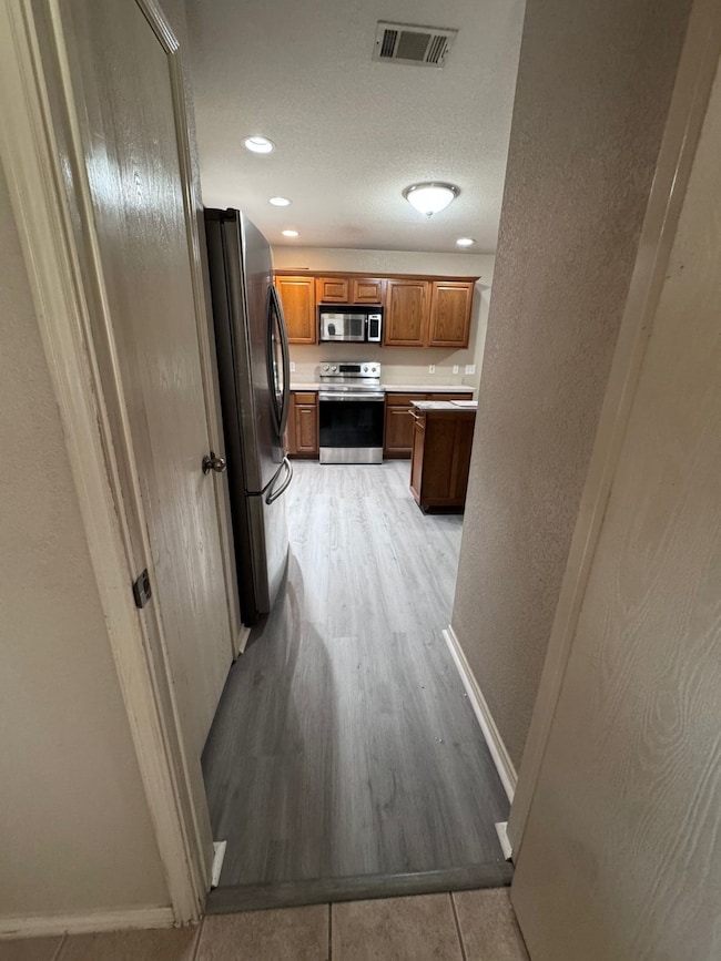 Kitchen featuring a textured wall, appliances with stainless steel finishes, light countertops, brown cabinets, and light tile patterned flooring