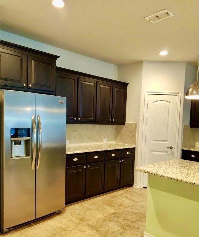 Kitchen with dark brown cabinets, pendant lighting, light tile patterned floors, decorative backsplash, and stainless steel refrigerator with ice dispenser