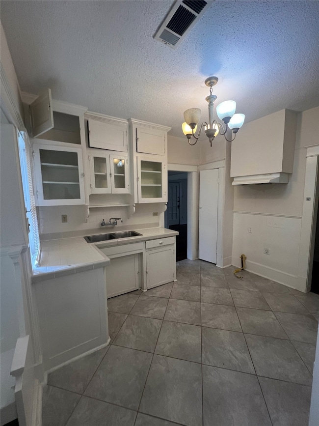 Kitchen featuring white cabinetry, a chandelier, a textured ceiling, glass insert cabinets, and light tile patterned floors