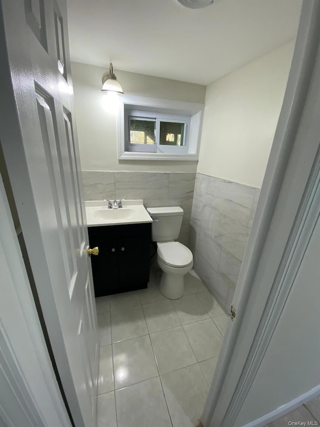 Bathroom with tile walls, vanity, light tile patterned floors, and wainscoting