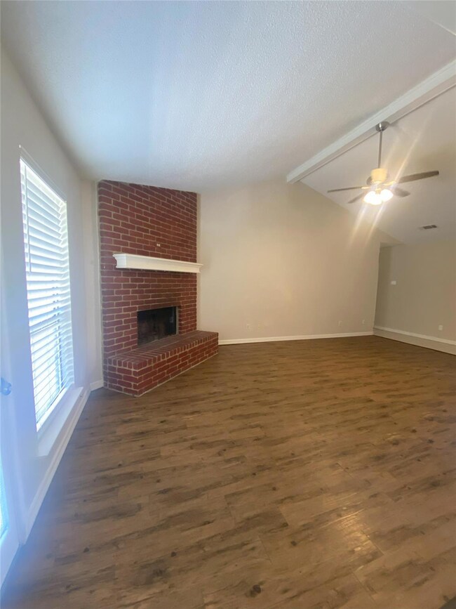 Unfurnished living room with dark wood-type flooring, vaulted ceiling with beams, ceiling fan, a textured ceiling, and a fireplace