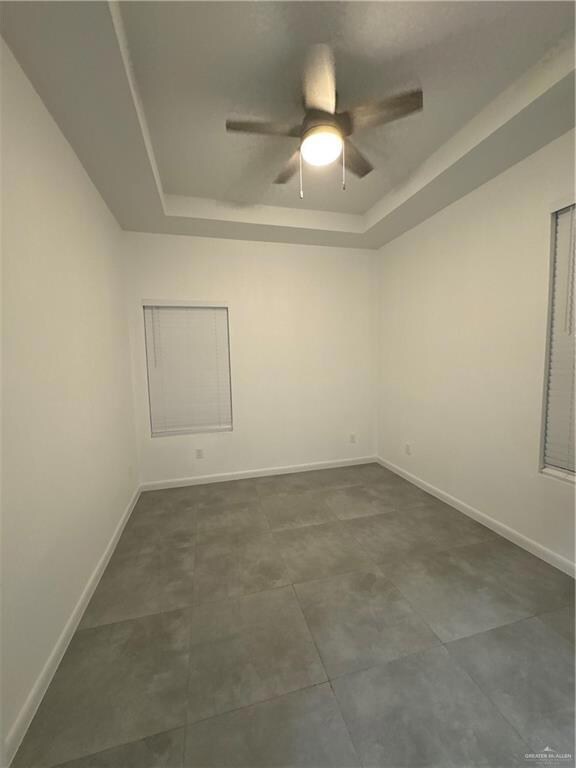 Spare room featuring a raised ceiling, ceiling fan, and baseboards