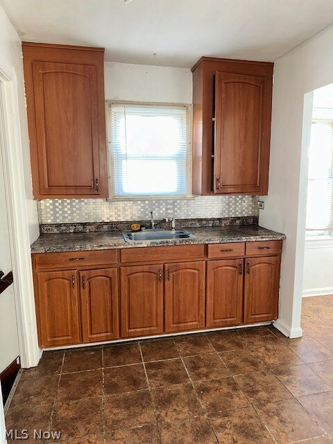 Kitchen featuring dark stone counters, dark tile flooring, sink, and backsplash
