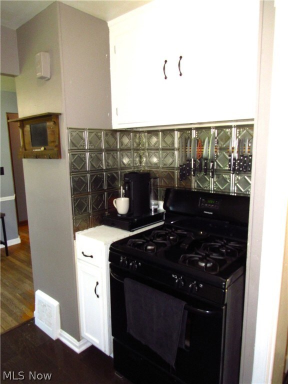 Kitchen with black gas range oven, white cabinetry, backsplash, and dark hardwood / wood-style flooring
