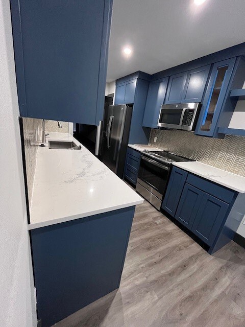 Kitchen with blue cabinetry, glass insert cabinets, decorative backsplash, light stone countertops, and stove