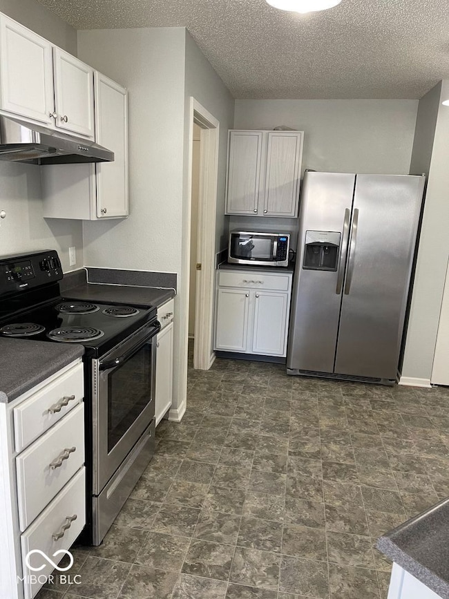 kitchen with appliances with stainless steel finishes, under cabinet range hood, a textured ceiling, white cabinetry, and dark countertops