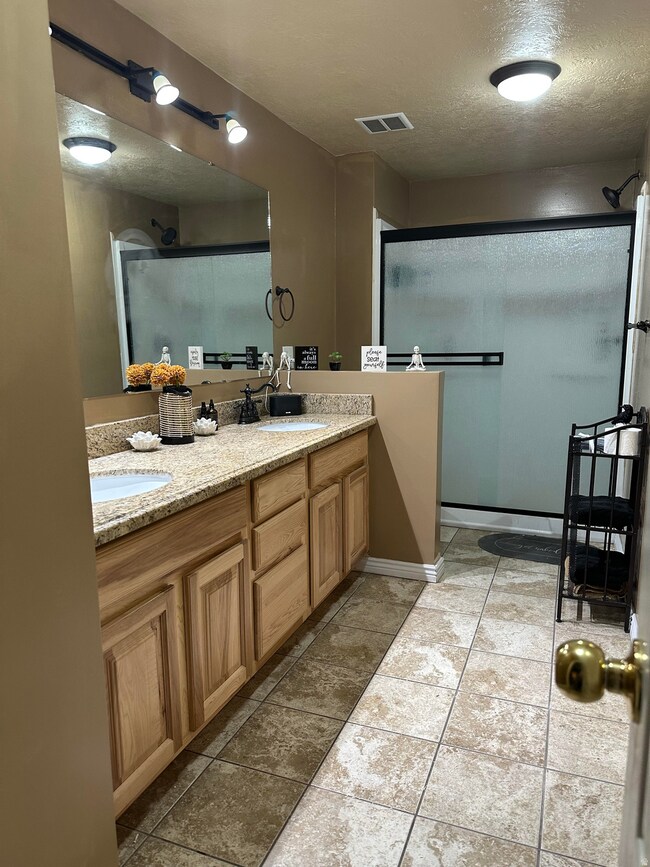 Bathroom featuring a textured ceiling, double vanity, a shower stall, and dark tile patterned flooring