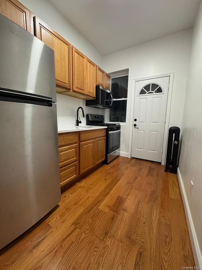 Kitchen featuring appliances with stainless steel finishes, light countertops, dark wood-style flooring, and brown cabinetry