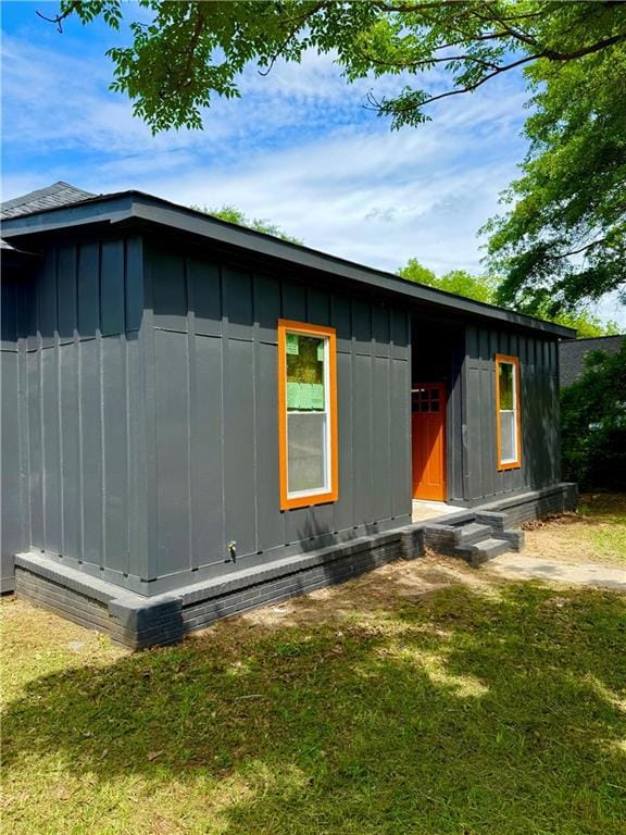 View of side of property with board and batten siding, a lawn, and entry steps