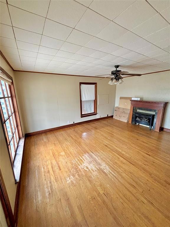 Unfurnished living room with light wood-type flooring, a glass covered fireplace, a ceiling fan, and a paneled ceiling