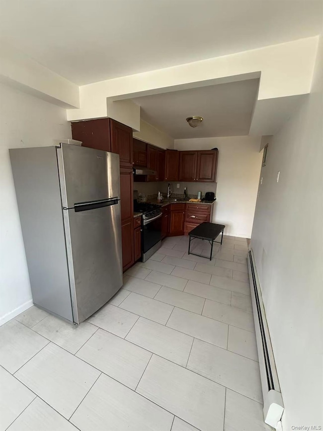 Kitchen with appliances with stainless steel finishes, a baseboard heating unit, under cabinet range hood, and light tile patterned floors