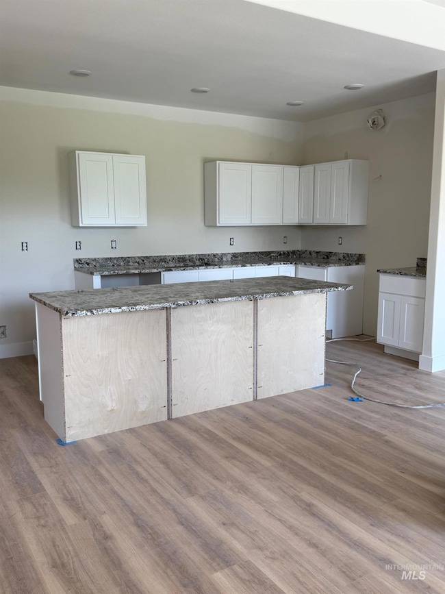 Kitchen featuring dark stone countertops, white cabinets, light wood finished floors, and a center island
