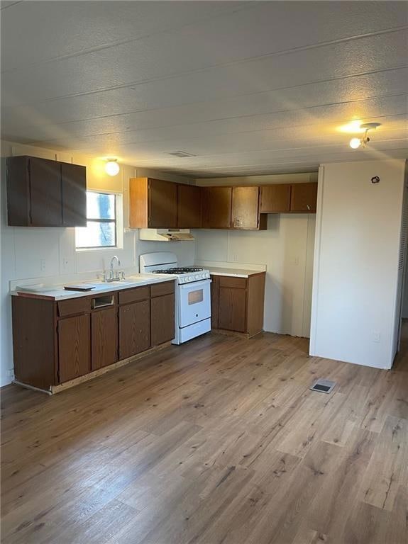 Kitchen with light countertops, dark wood-type flooring, white range with gas cooktop, brown cabinets, and a textured ceiling
