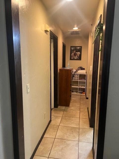 Hall featuring light tile patterned flooring, a textured wall, and baseboards
