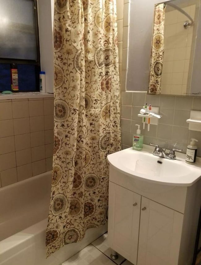 Bathroom featuring vanity, shower / bath combo with shower curtain, and tile walls