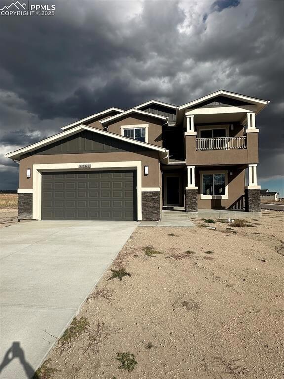 Craftsman house with stucco siding, stone siding, driveway, and a balcony