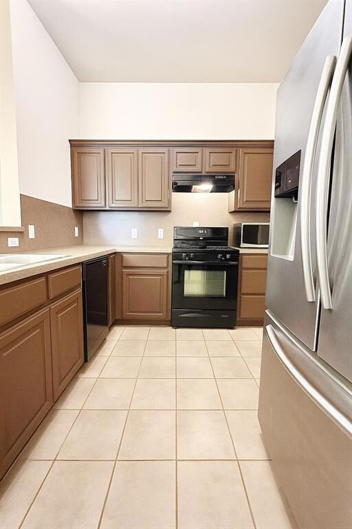 Kitchen with black appliances, under cabinet range hood, light countertops, and light tile patterned floors